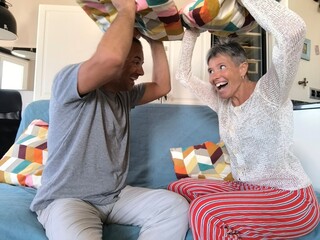 Happy couple plays with pillows on the sofa in their home.  The girl takes a pillow to throw at her...