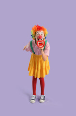 Funny little girl dressed as clown shouting into megaphone on lilac background. April Fools' Day celebration