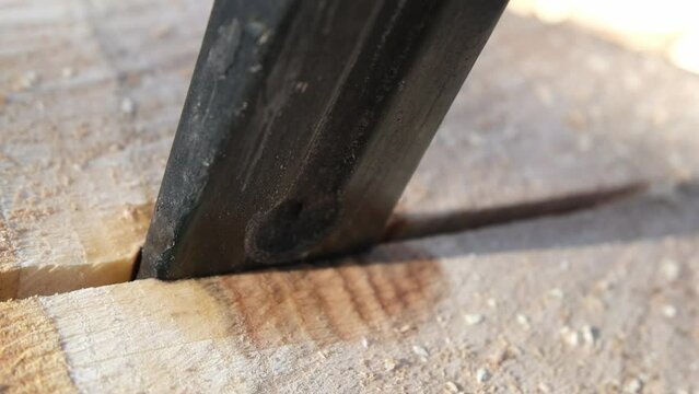 Extreme close up of iron wedge impaled into oak log crack ready to be split while mowing camera away exposing firewood and stumps covered in snow.
