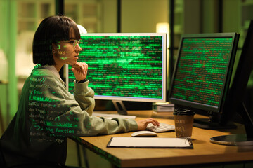Thoughtful female programmer with projection of programming code working in office at night