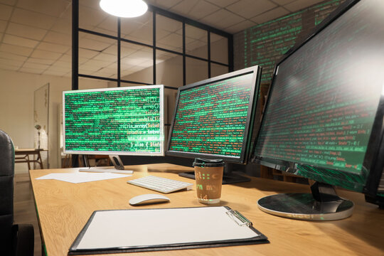 Computer monitors with programming code on table in dark office at night