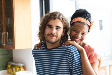 Fotobehang A diverse couple shares a warm embrace at home, smiling contentedly © WavebreakMediaMicro