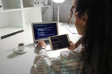 Female African-American programmer working with laptop and tablet computer in office at night - obrazy, fototapety, plakaty