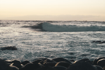 Playa al atardecer con olas rompiendo en las rocas