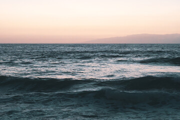 Playa al atardecer con olas rompiendo en las rocas