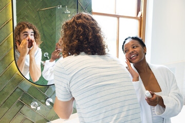 A diverse couple engages in their morning skincare routine in the bathroom at home