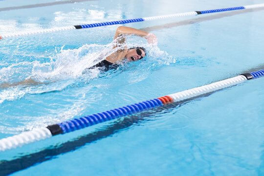 A Caucasian female athlete swimmer is swimming laps in a pool, blue background