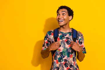 Photo portrait of young smiling positive guy in t shirt bring backpack look empty space tour excursion isolated on yellow color background - obrazy, fototapety, plakaty