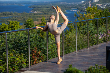A young woman in a tracksuit performs physical exercises in a summer park