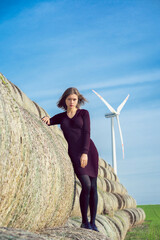 A girl with hair flying in the wind stands on a haystack