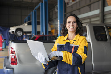 portrait young caucasian female in uniform working at garage service, professional woman technician using laptop diagnostic check a car for repair