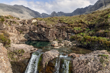 The Fairy Pools unveil a tranquil cascade, its waters merging with a still, clear pond against the...