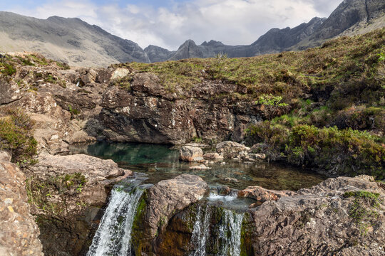 The Fairy Pools unveil a tranquil cascade, its waters merging with a still, clear pond against the backdrop of Isle of Skye imposing Cuillin range