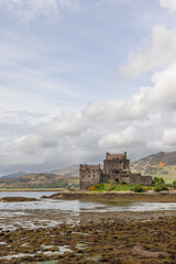 Eilean Donan Castle, poised on the edge of a loch, showcases the rugged beauty and heritage of the Highlands, with a serene sky and low tide revealing the algae-covered shore (Vertical photo)