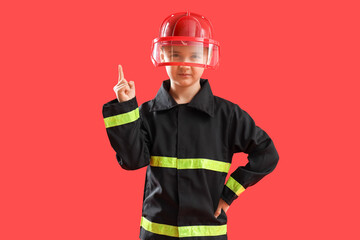 Cute little firefighter pointing at something on red background