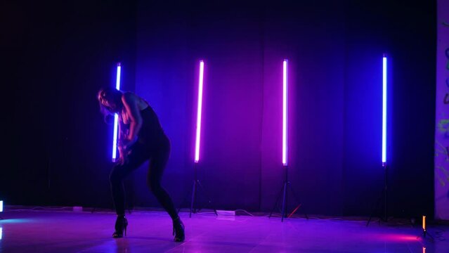 Silhouette of woman dancing under neon lights. Vibrant neon lit dance floor with woman in motion. Energetic dance performance in dark room with neon glow. Ecstatic female dancer surrounded by neon lig