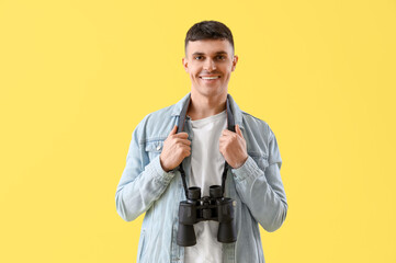 Young man with binoculars on yellow background