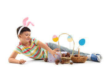 Cute little boy in bunny ears headband with baskets of chocolate eggs, gift box and decor for...