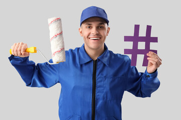 Handsome male painter with paint roller and hashtag sign on grey background
