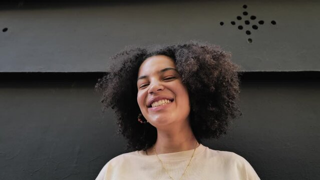 Young woman with curly hair on the black background looking at camera laughing
