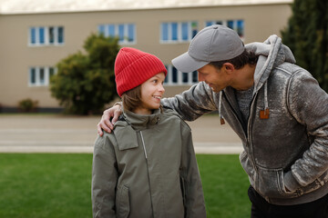 Fototapeta premium Male school teacher giving advice to teenage smiling boy at school yard, Teacher's wisdom: Smiling boy receives valuable advice from his male school teacher outdoors.