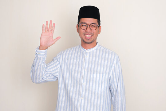 Moslem Asian man smiling happy and waving hand at the camera