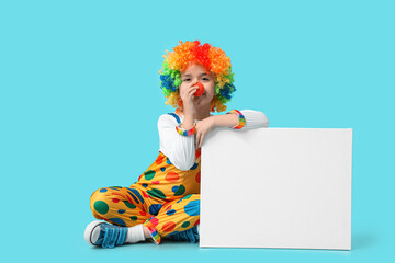 Funny little boy in clown costume with blank poster sitting on blue background. April Fools Day celebration