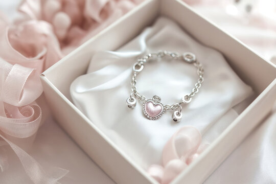 Delicate silver bracelet with a heart charm presented in a luxurious white box among soft pink ribbons