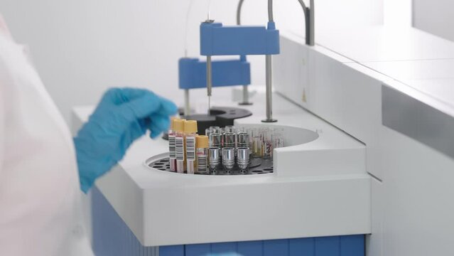 A female scientist places blood samples into a modern automatic device to analyze blood biochemical parameters. A professional chemist works in a biotechnology laboratory.