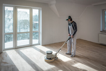 Professional worker polishing sanding parquet floor with orbital polishing machine
