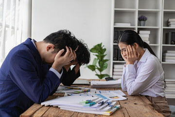 Very tired, stressed and busy business people sitting at the office table, holding their heads and ignoring a lot of business documents on the table, unsuccessful business concept. - obrazy, fototapety, plakaty