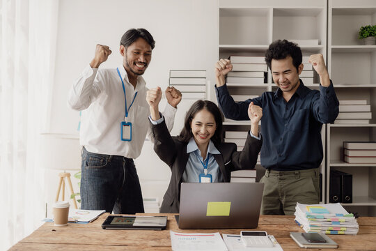 A team of young Asian businessmen met to express their happiness about the project's success by clapping along with computers in a shared office space and celebrating the victory.