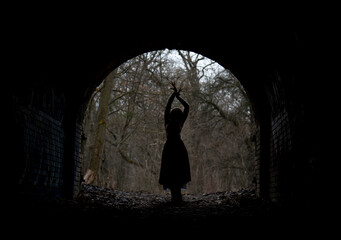 dark silhouette of dramatic lonely single woman in stone arch in winter forest - obrazy, fototapety, plakaty