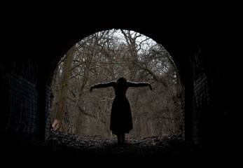 dark silhouette of dramatic lonely single woman in stone arch in winter forest