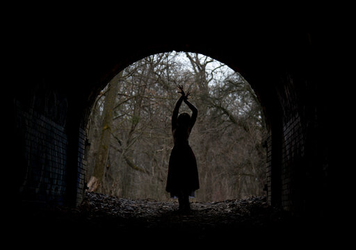 dark silhouette of dramatic lonely single woman in stone arch in winter forest