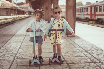 Two little girls having fun with scooters. Sisters play outdoors with scooters. - 763320340