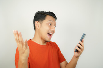 Fototapeta premium Asian man in orange t-shirt happy looking at what's on smartphone on isolated background