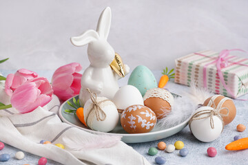 Plate with decorated Easter eggs, toy bunny and tulips on white background