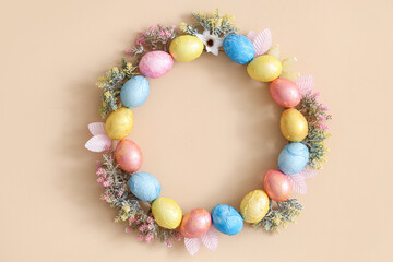 Wreath made from Easter eggs and flowers hanging on beige wall, closeup