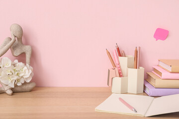 Stationery and figurine with flowers on wooden table near pink wall - obrazy, fototapety, plakaty