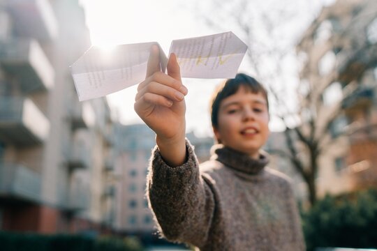 A 10 year old boy launches a paper airplane on a sunny day