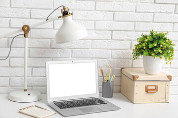 Stylish workplace with laptop, white lamp and houseplant near white brick wall