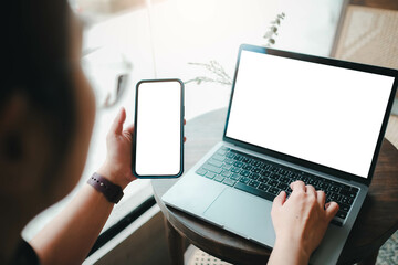 Close-up image of a woman sitting in the cafe and using her smartphone and laptop. smartphone and laptop white blank screen mockup for display your graphic banner.