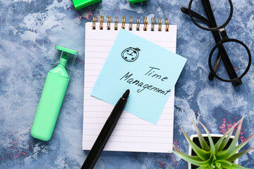 Text TIME MANAGEMENT with notebook, glasses and felt-tip pen on blue background. Top view