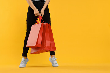 Woman with shopping bags on yellow background, closeup. Space for text - obrazy, fototapety, plakaty