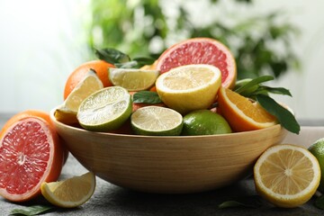 Different fresh citrus fruits and leaves on table against blurred background, closeup