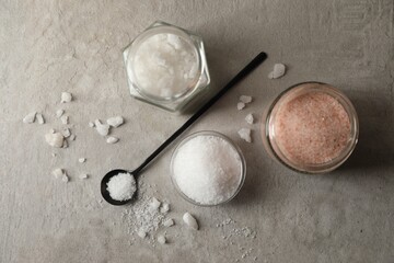 Different natural salt on grey textured table, flat lay