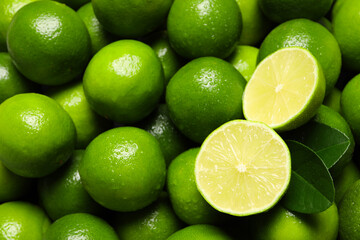 Fresh limes and leaves with water drops as background, top view