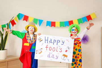 Fototapeta premium Funny little children in clown costumes with poster at home. April Fools' Day celebration