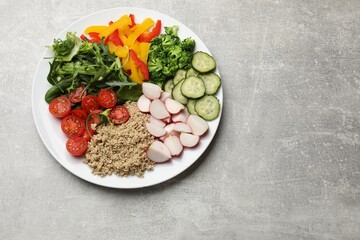 Fototapeta na wymiar Vegetarian diet. Plate with tasty vegetables and quinoa on light grey table, top view. Space for text
